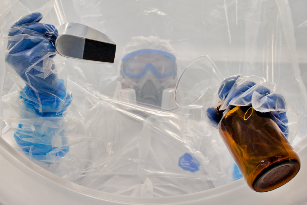 Gloved and masked person working in laboratory.